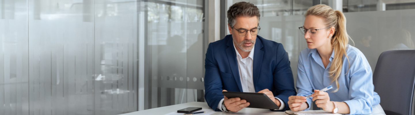 Two business professionals reviewing documents on a digital tablet during a meeting.