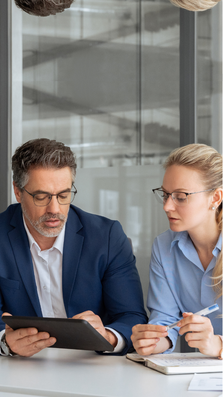 Two business professionals reviewing documents on a digital tablet during a meeting.
