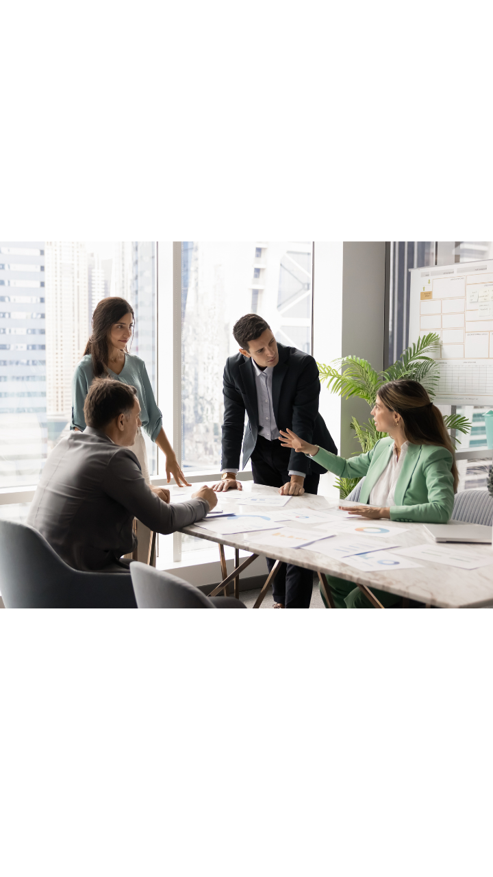 Four business professionals reviewing and discussing documents in a modern meeting room.