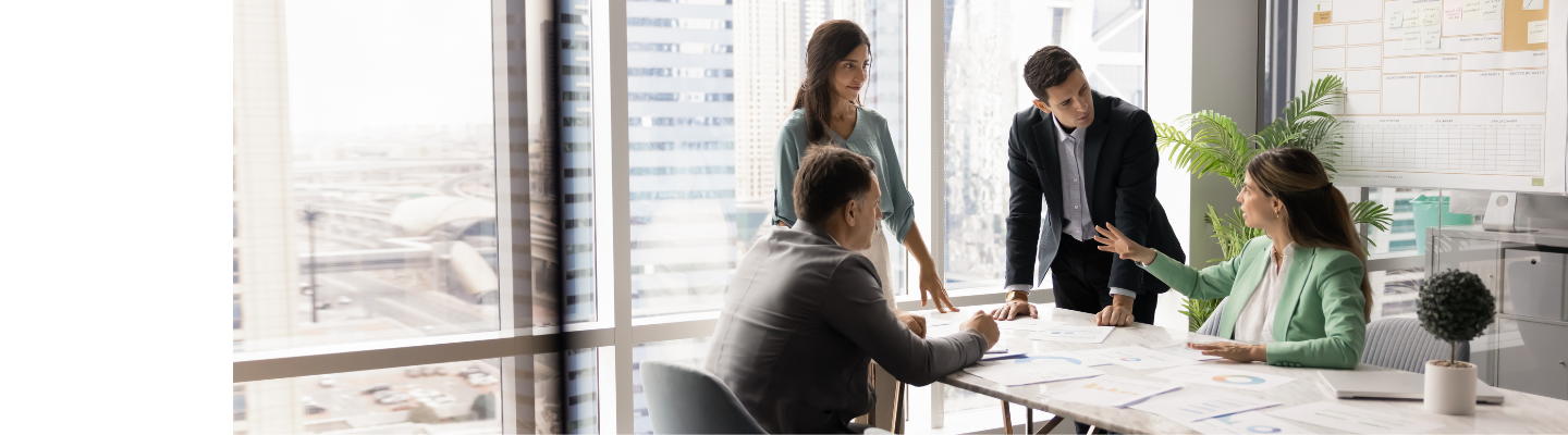 Four business professionals reviewing and discussing documents in a modern meeting room.